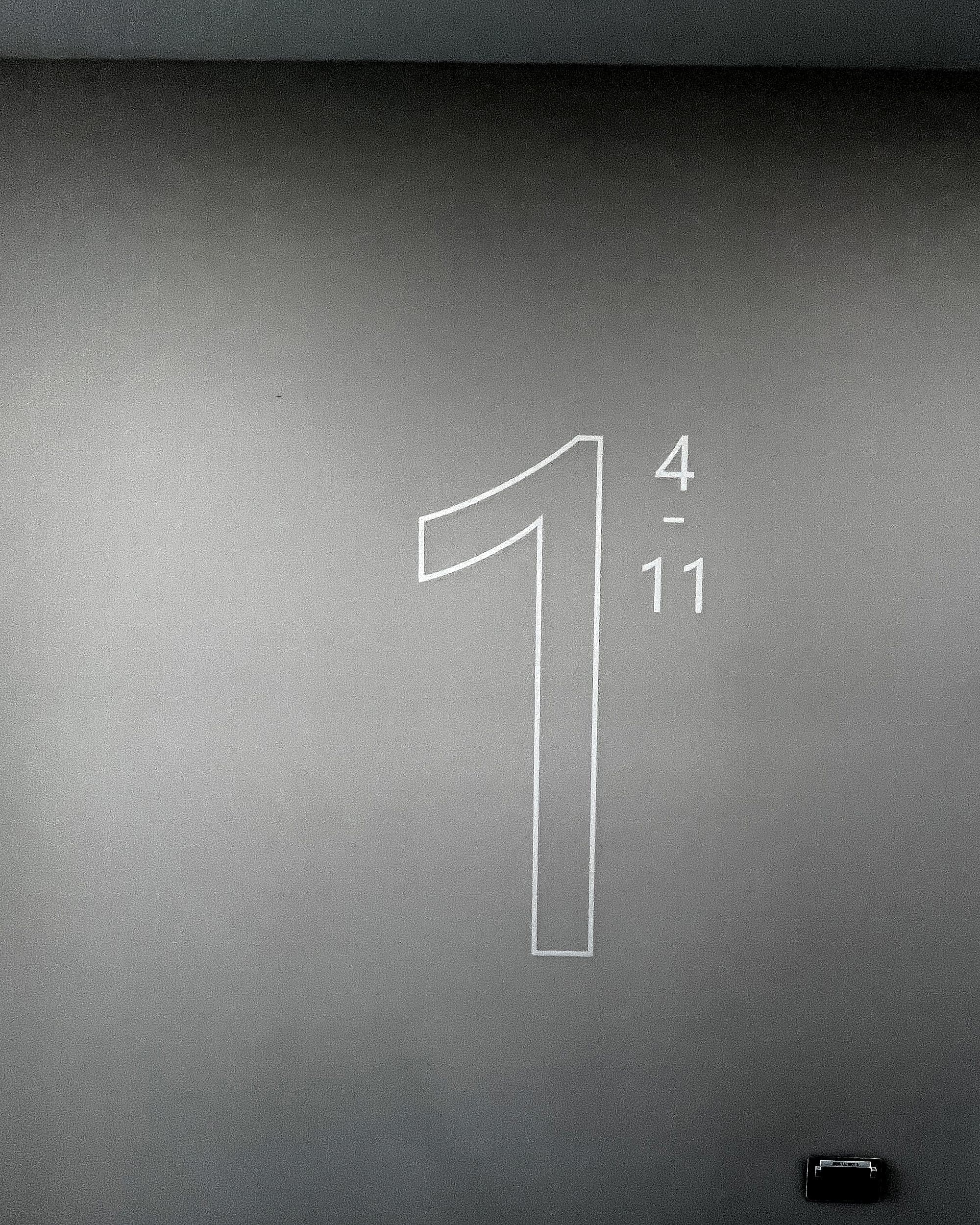 Large outline floor numeral one with the apartment range four to eleven beside it at Churchfields, applied directly to a plastered lobby wall with no panel or frame