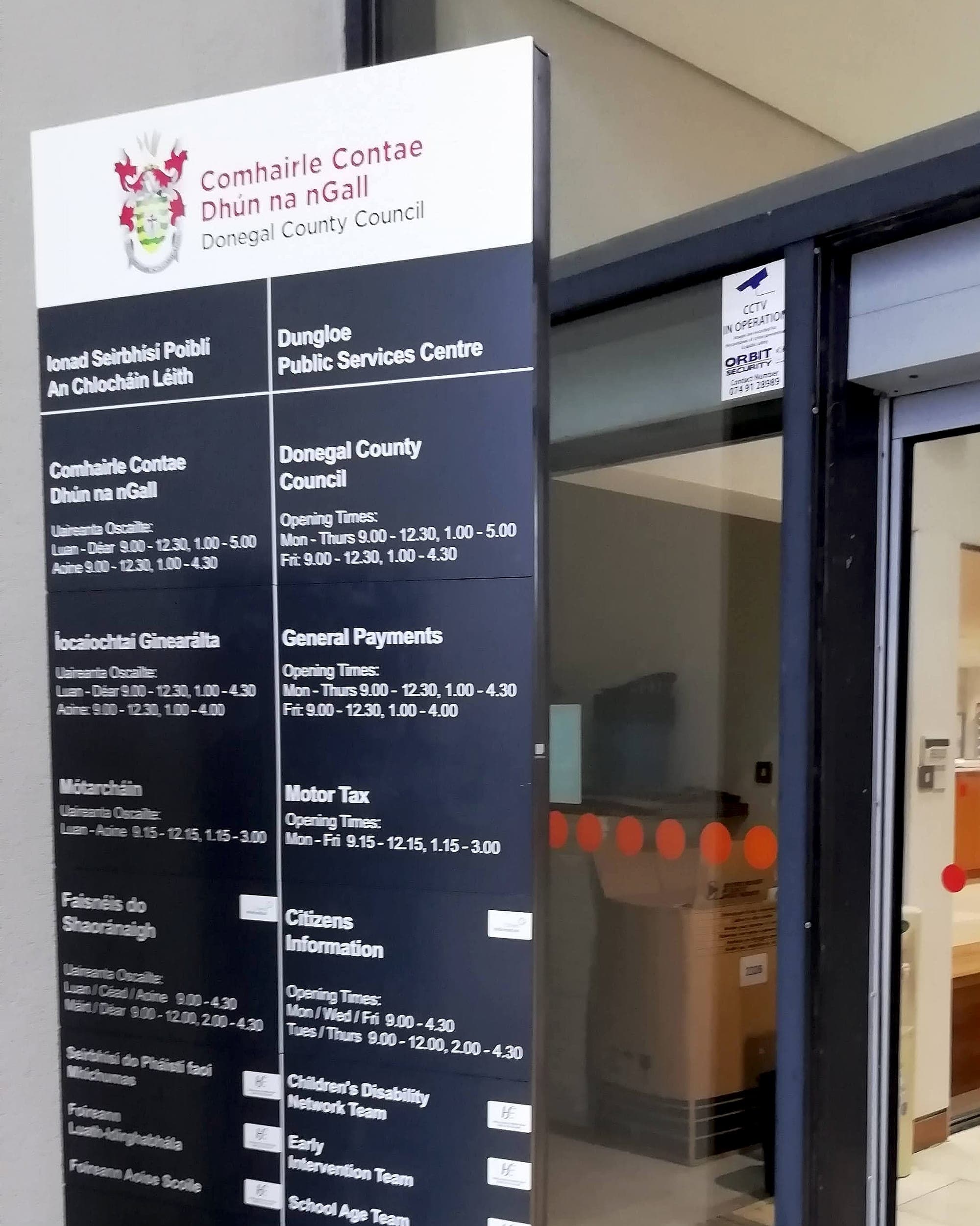 Bilingual external totem at Donegal County Council's Dungloe Public Services Centre listing council services, general payments, motor tax, Citizens Information and children's disability teams with opening times in Irish and English