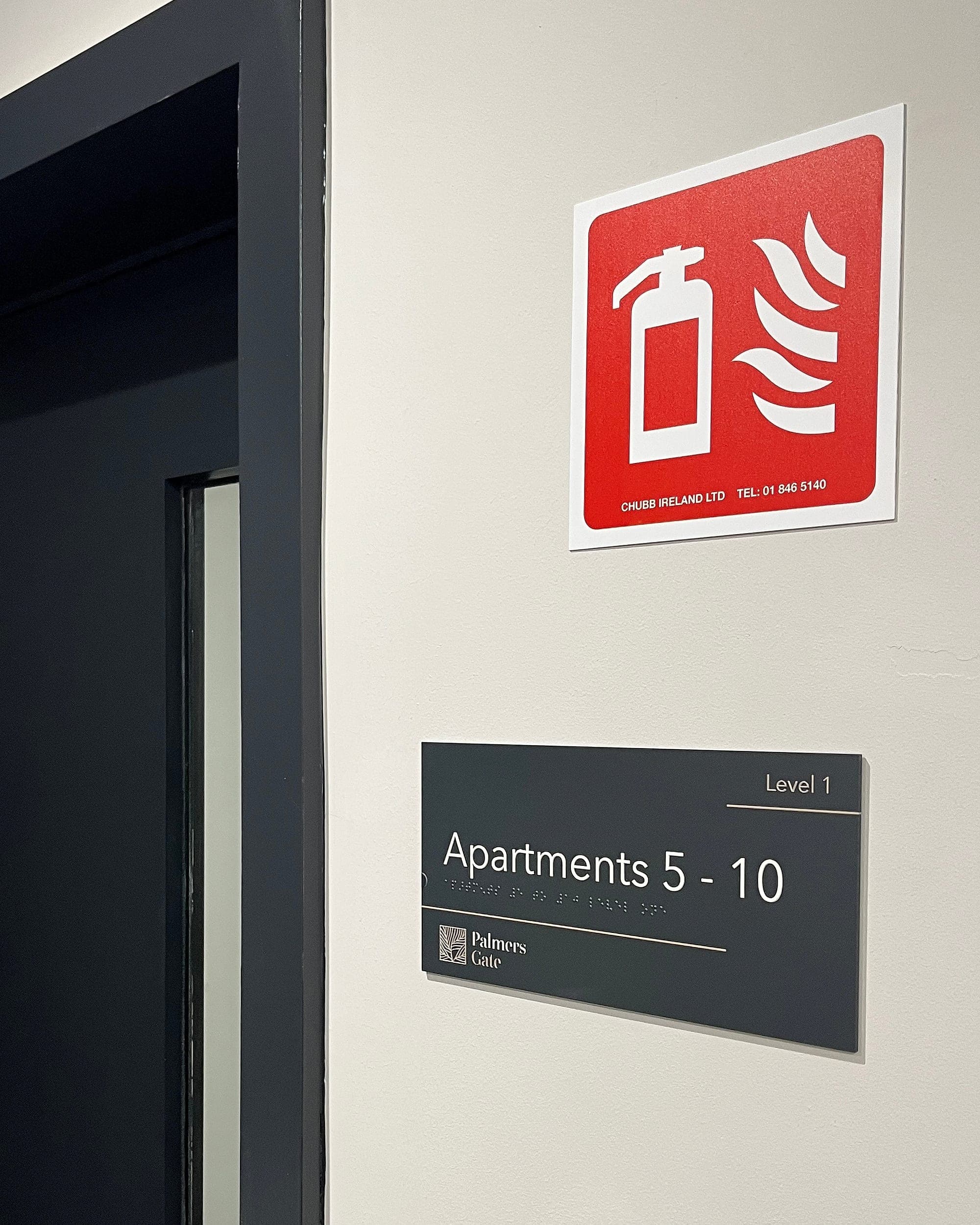 Palmers Gate: stair core level identification sign reading Apartments 5-10, Level 1 with braille, mounted beside a fire door beneath a red fire extinguisher location sign