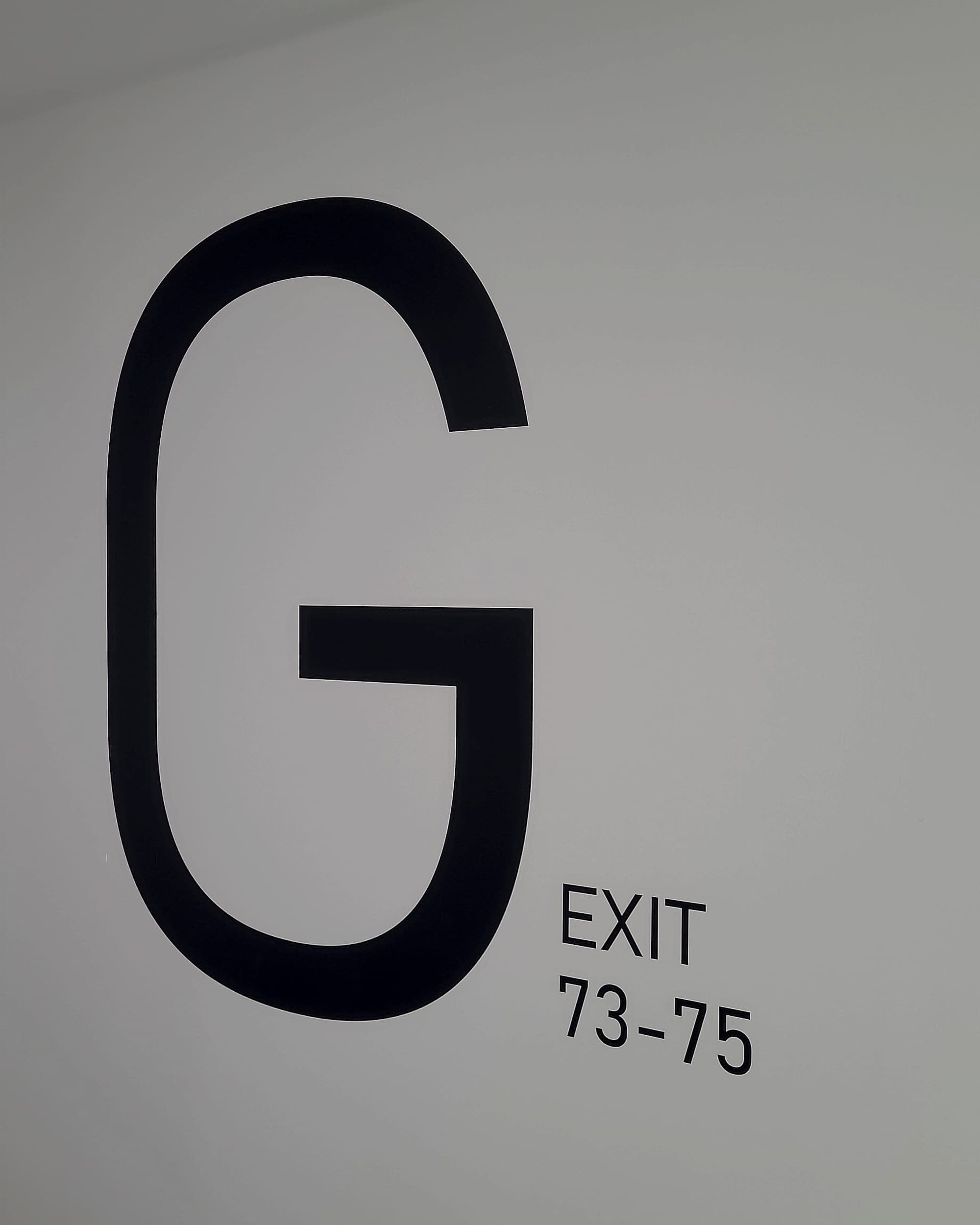 Level identification at architectural scale. A student accommodation floor supergraphic: an oversized letter G applied to a corridor wall with EXIT and the room range 73-75 set beside it
