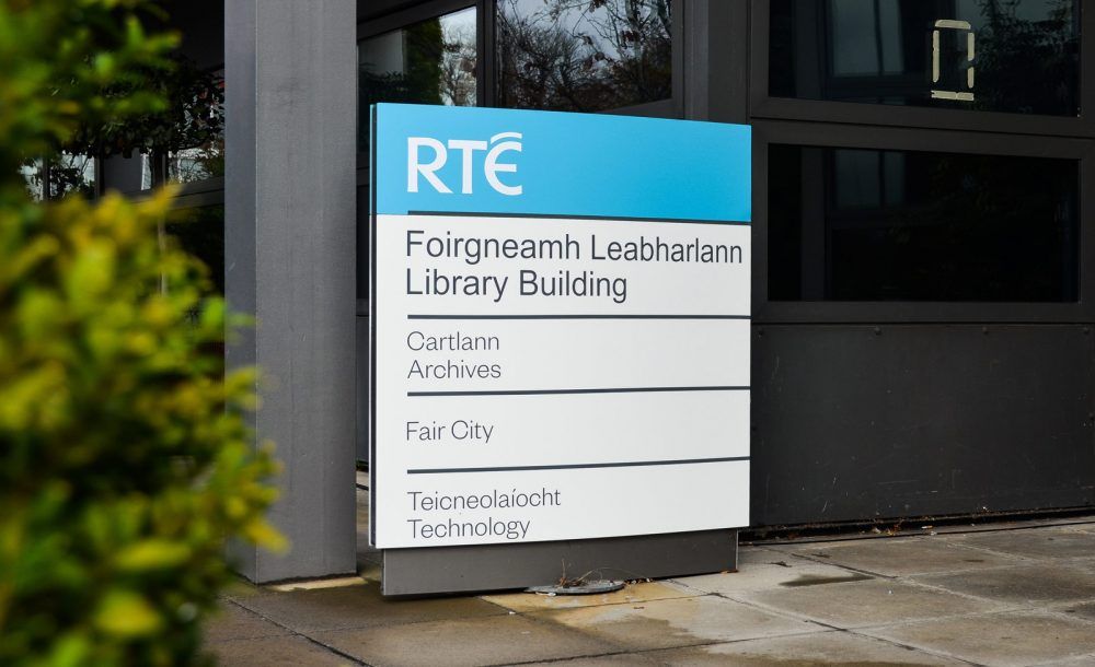 RTÉ building directory at the Library Building entrance, the RTÉ mark on a blue header above Archives, Fair City and Technology listed in Irish and English