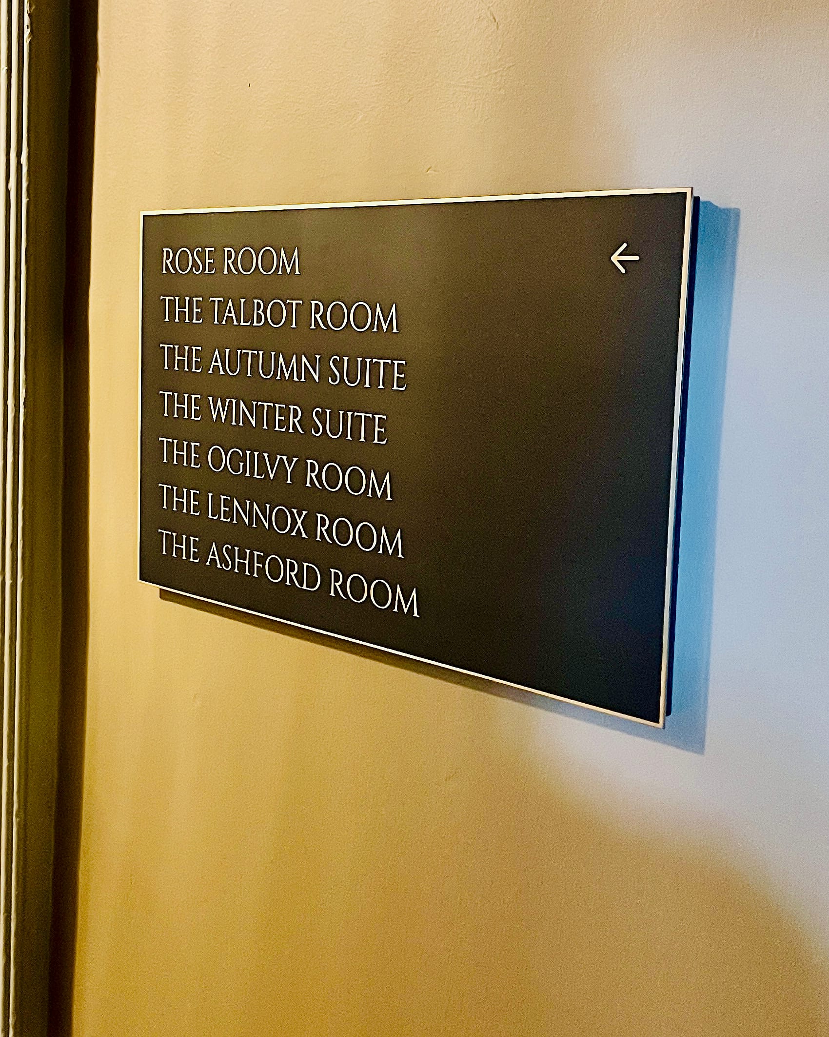 Directional wall sign at Carton House listing seven named meeting rooms and suites with a left arrow, in light lettering on a dark panel with a metal border